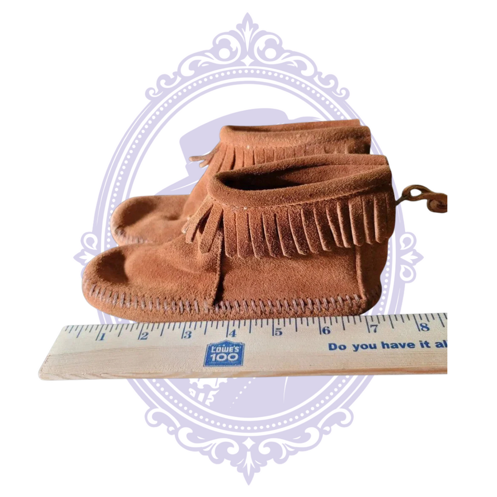 Front view of brown Minnetonka suede moccasin boots beside ruler