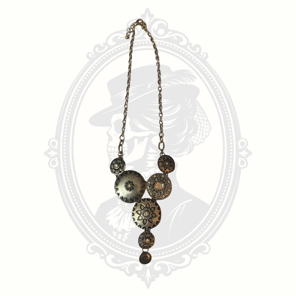 Long antiqued brass necklace with textured circular medallions and adjustable chain photographed on a soft gothic-inspired backdrop.