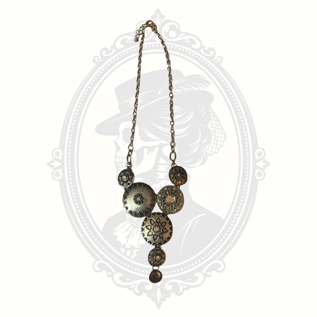 Long antiqued brass necklace with textured circular medallions and adjustable chain photographed on a soft gothic-inspired backdrop.