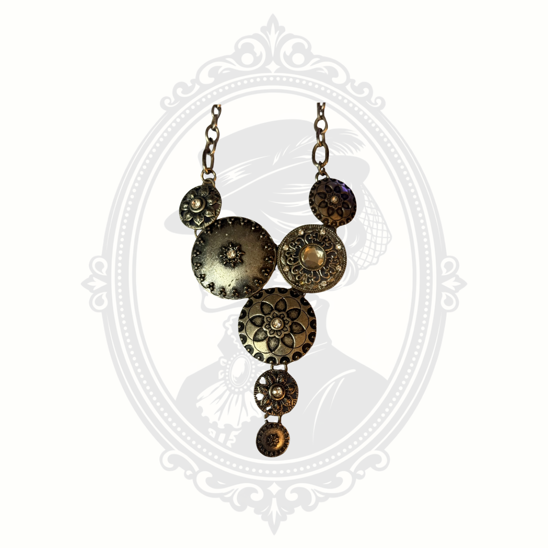 Antiqued brass statement necklace with layered medallions and floral-inspired detailing displayed against a gothic cameo background.