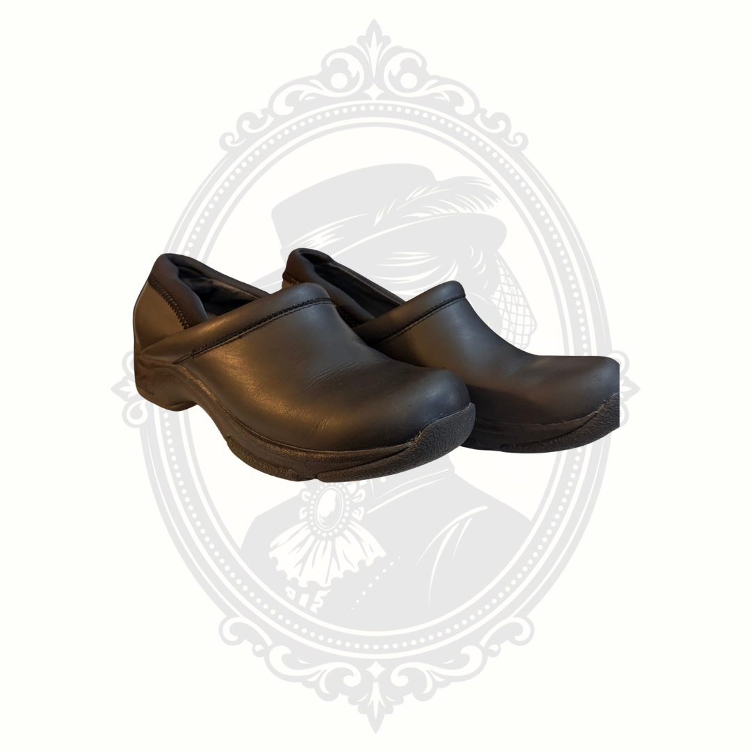 Black Dansko professional leather clogs viewed from front angle on gray background