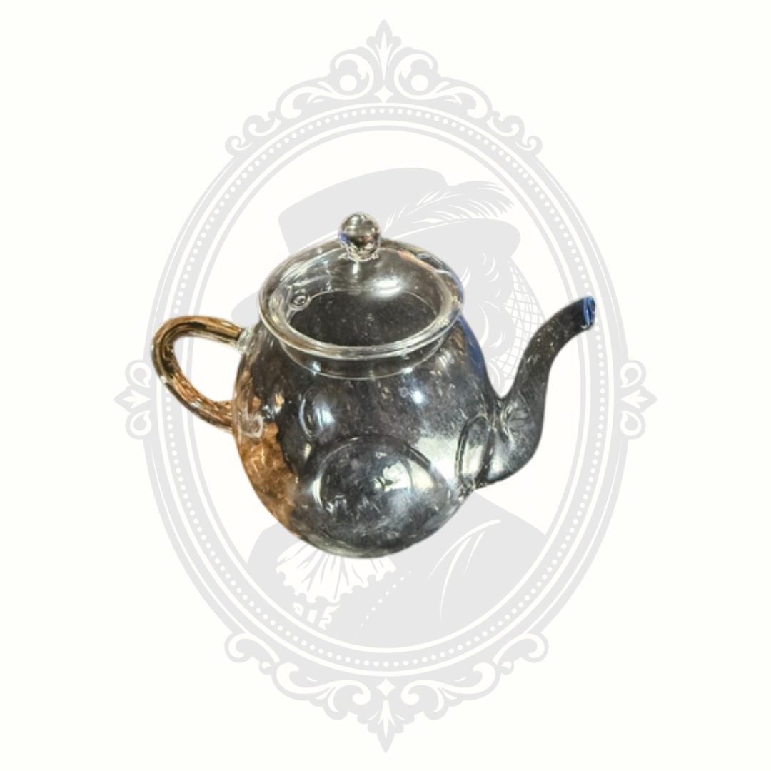 Clear glass Creano tea pot with long curved spout and fitted lid styled on Mrs. Bones Curio Cupboard branded backdrop.