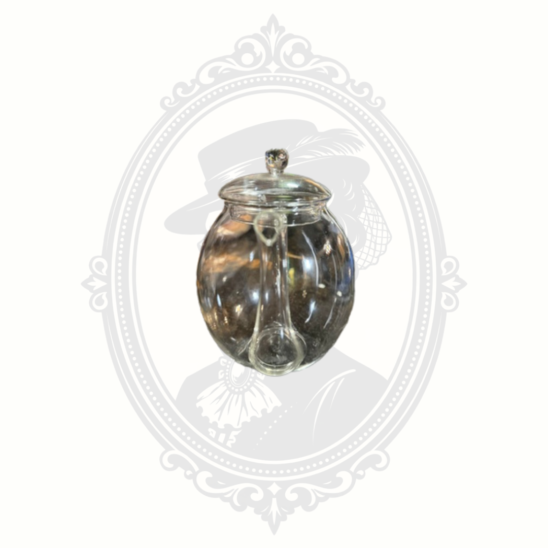 Front angle view of authentic Creano clear glass teapot with curved spout and fitted glass lid on branded gray background.
