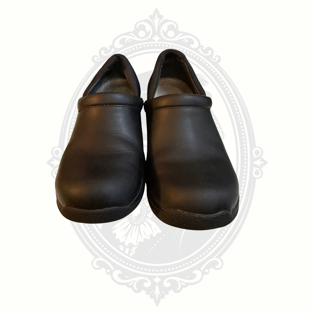 Black Dansko professional leather clogs viewed from front angle on gray background
