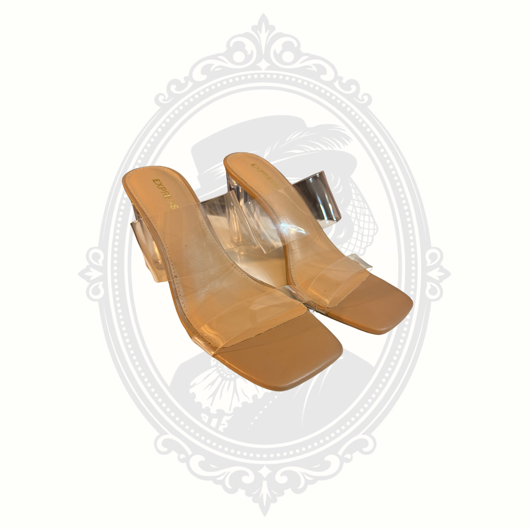 Express nude mule heels with transparent clear straps and sculptural clear block heels photographed against a neutral background.