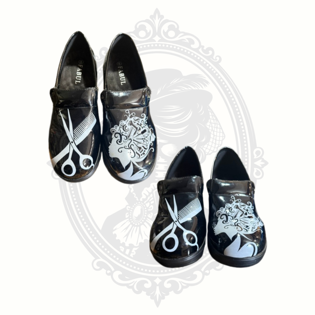 Top and angled views of black Fabul slip-on shoes with white cosmetology-inspired graphics including scissors and ornate salon motifs.