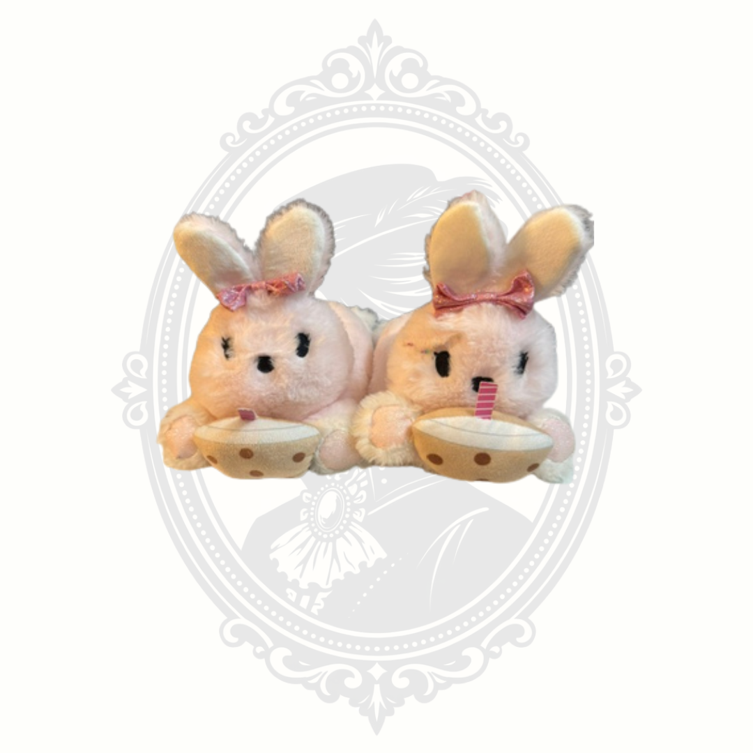 Front view of plush pink bunny slippers with embroidered faces and cocoa cups