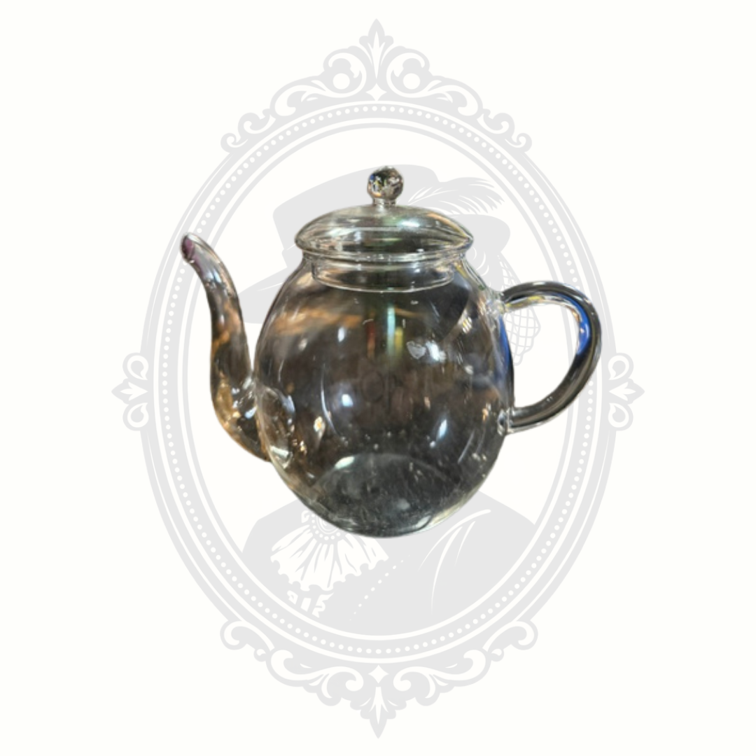 Clear glass Creano tea pot with long curved spout and fitted lid styled on Mrs. Bones Curio Cupboard branded backdrop.