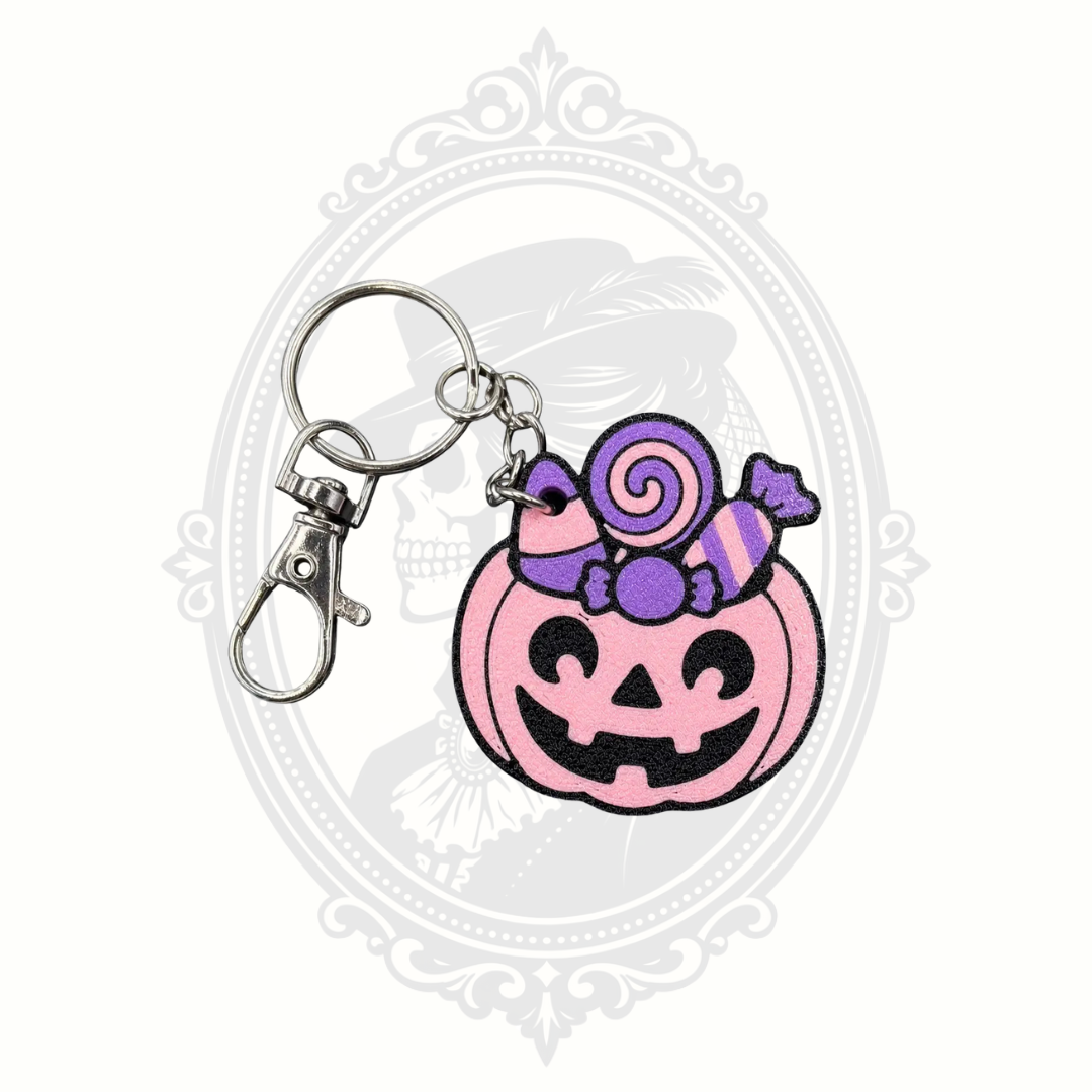 Pink Candy Pumpkin keychain featuring a smiling pink jack-o'-lantern topped with purple Halloween candy, metal keyring, and lobster clasp.
