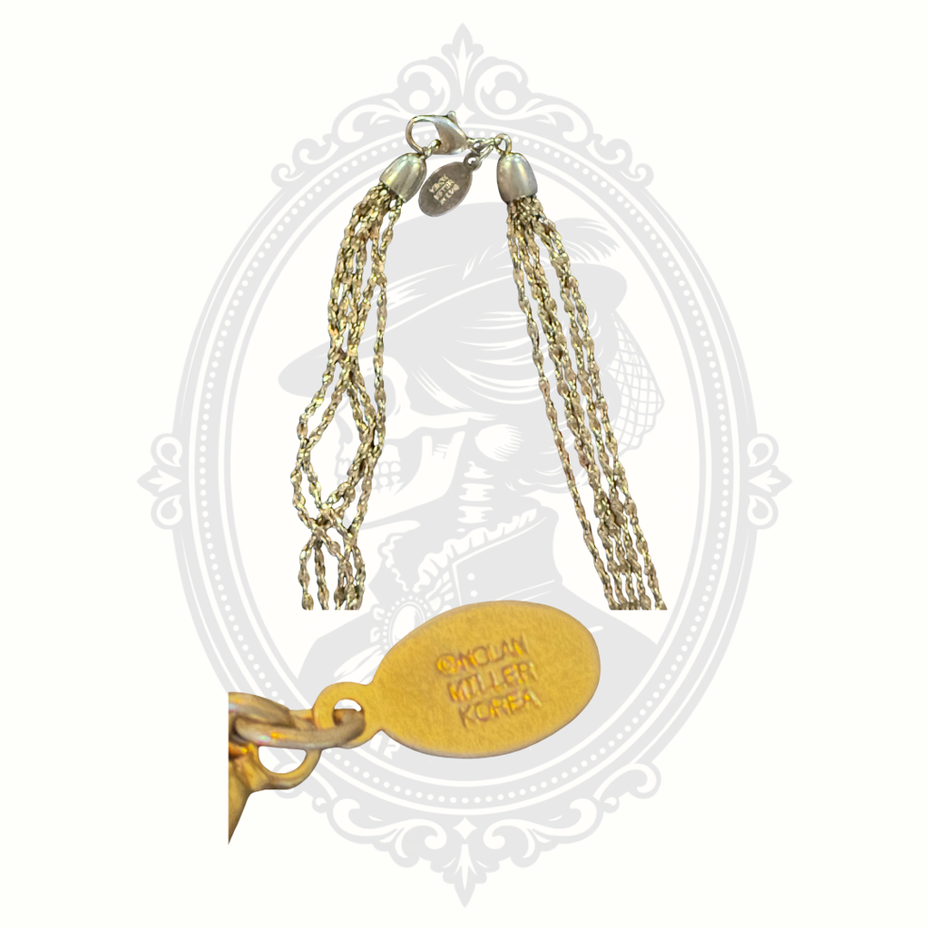 Close-up of the signed Nolan Miller Korea jewelry tag and clasp on a vintage gold-tone multi-strand necklace.
