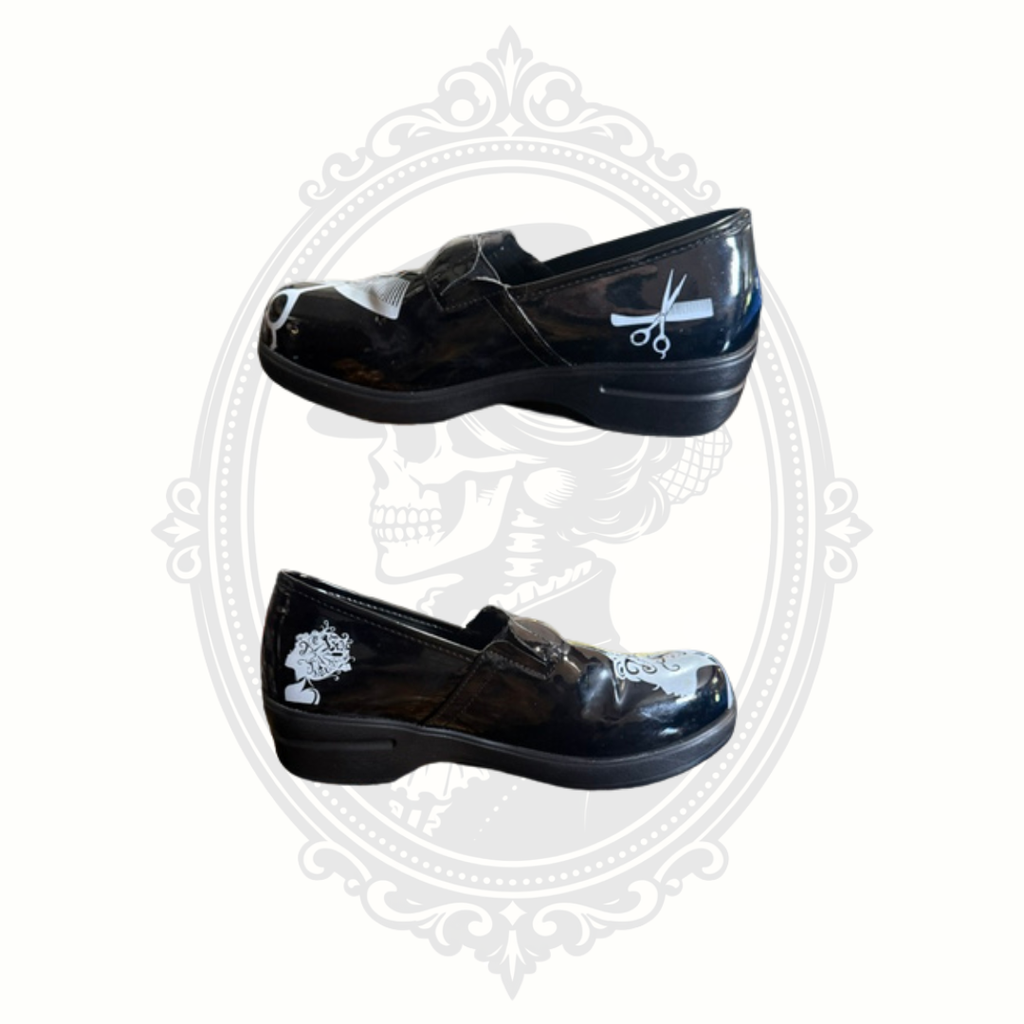 Black glossy slip-on shoes with white hairstylist graphics including scissors and salon artwork shown in side profile on gray gothic background.