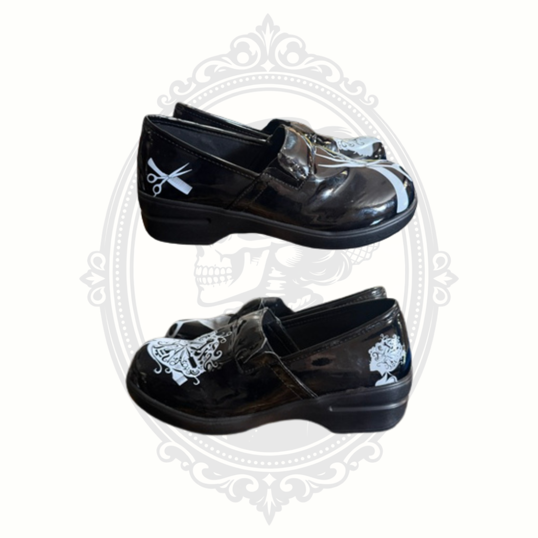 Pair of black stylist-themed slip-on shoes with white salon graphics and low comfort heels photographed from side angles.