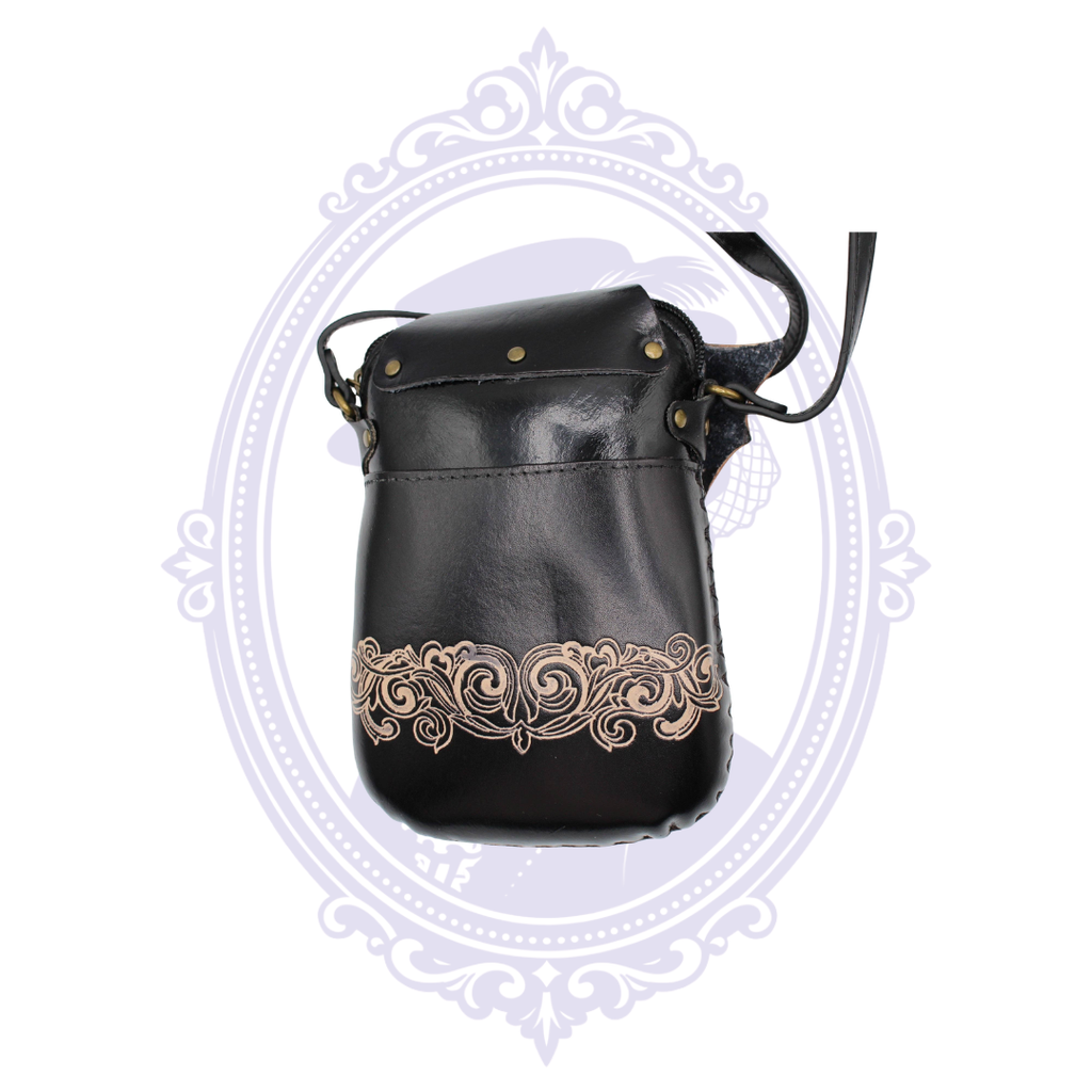 Back of black leather bat crossbody bag with ornate tan scrollwork and antique brass-tone hardware