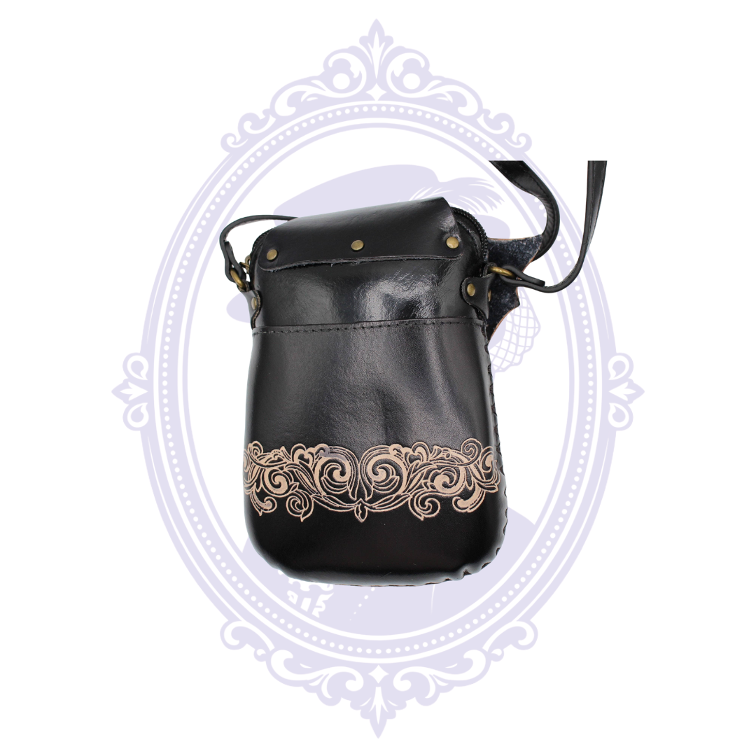 Back of black leather bat crossbody bag with ornate tan scrollwork and antique brass-tone hardware
