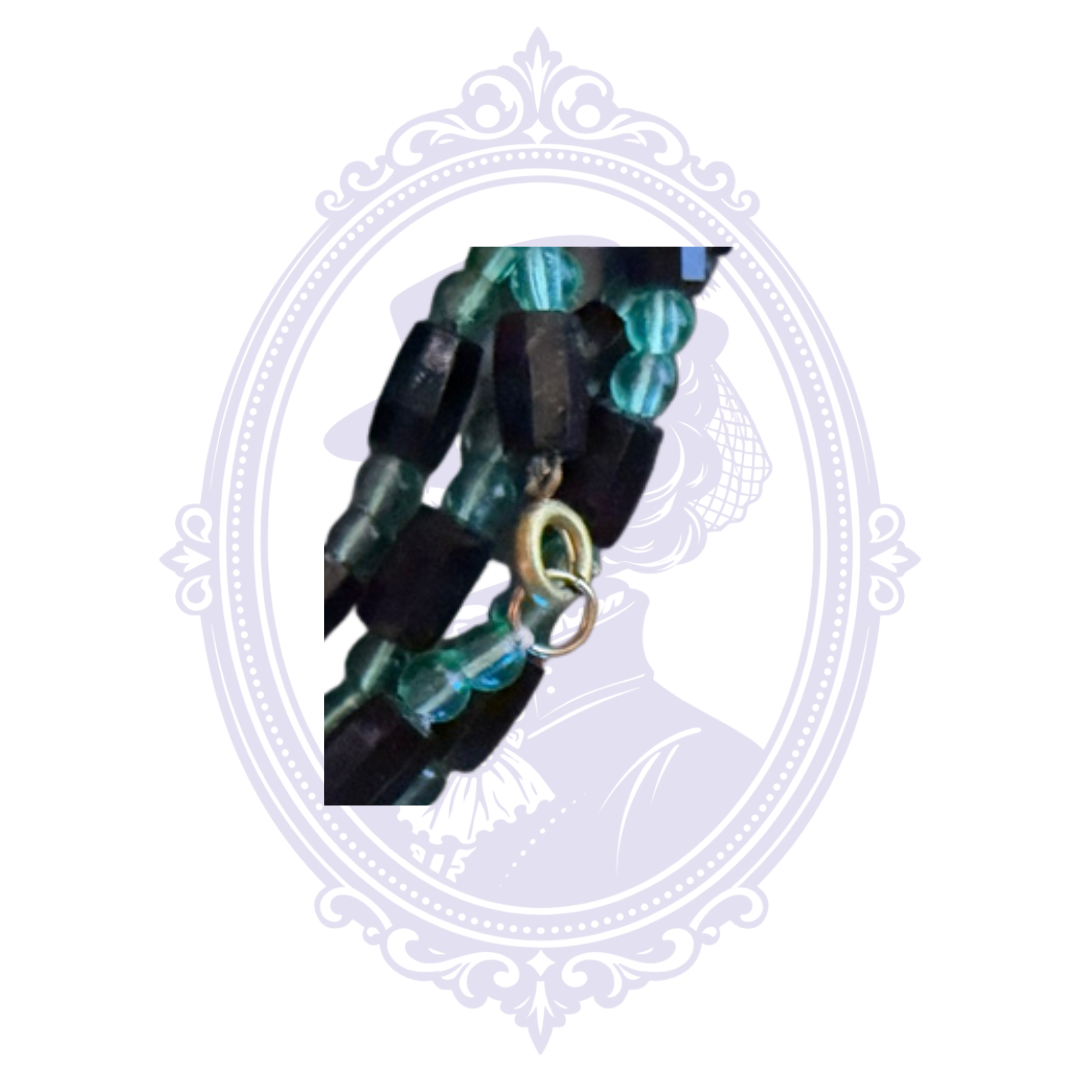 Close-up of black and teal multi-strand beaded necklace showing metal connecting rings and bead details.