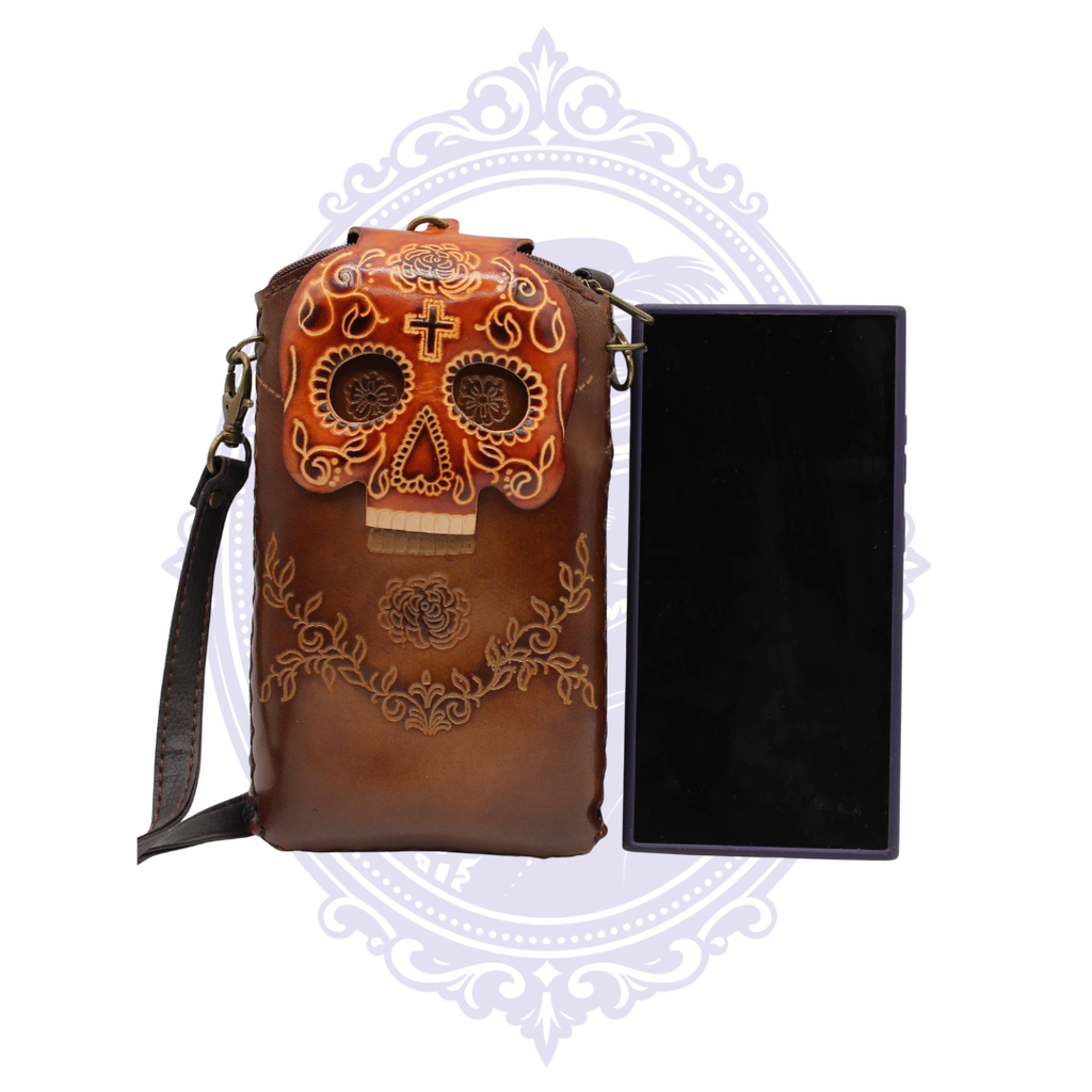 Brown genuine leather sugar skull cell phone crossbody holder shown beside a card-sized object for scale.