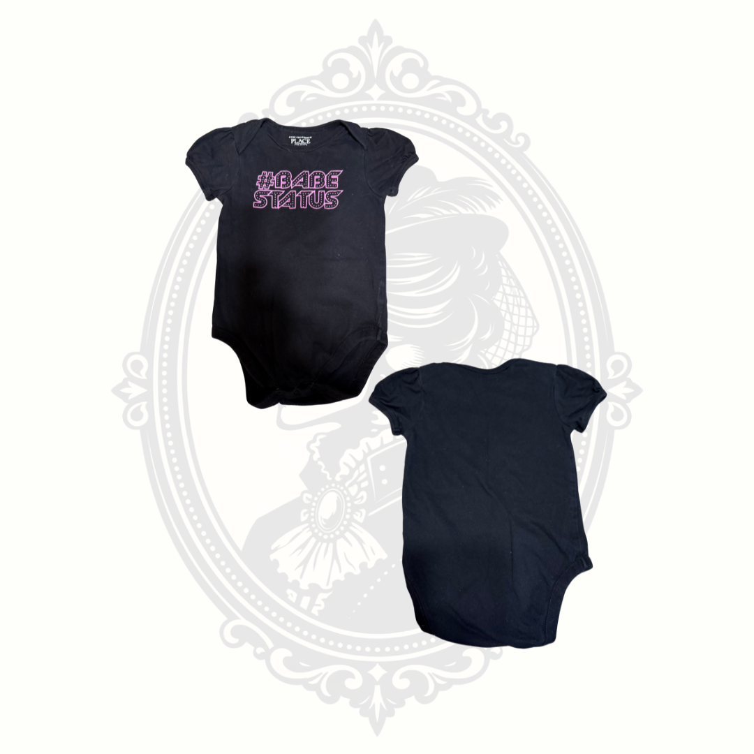 Black baby onesie from The Children’s Place featuring pink “#Babe Status” graphic on front with back view shown beside it.
