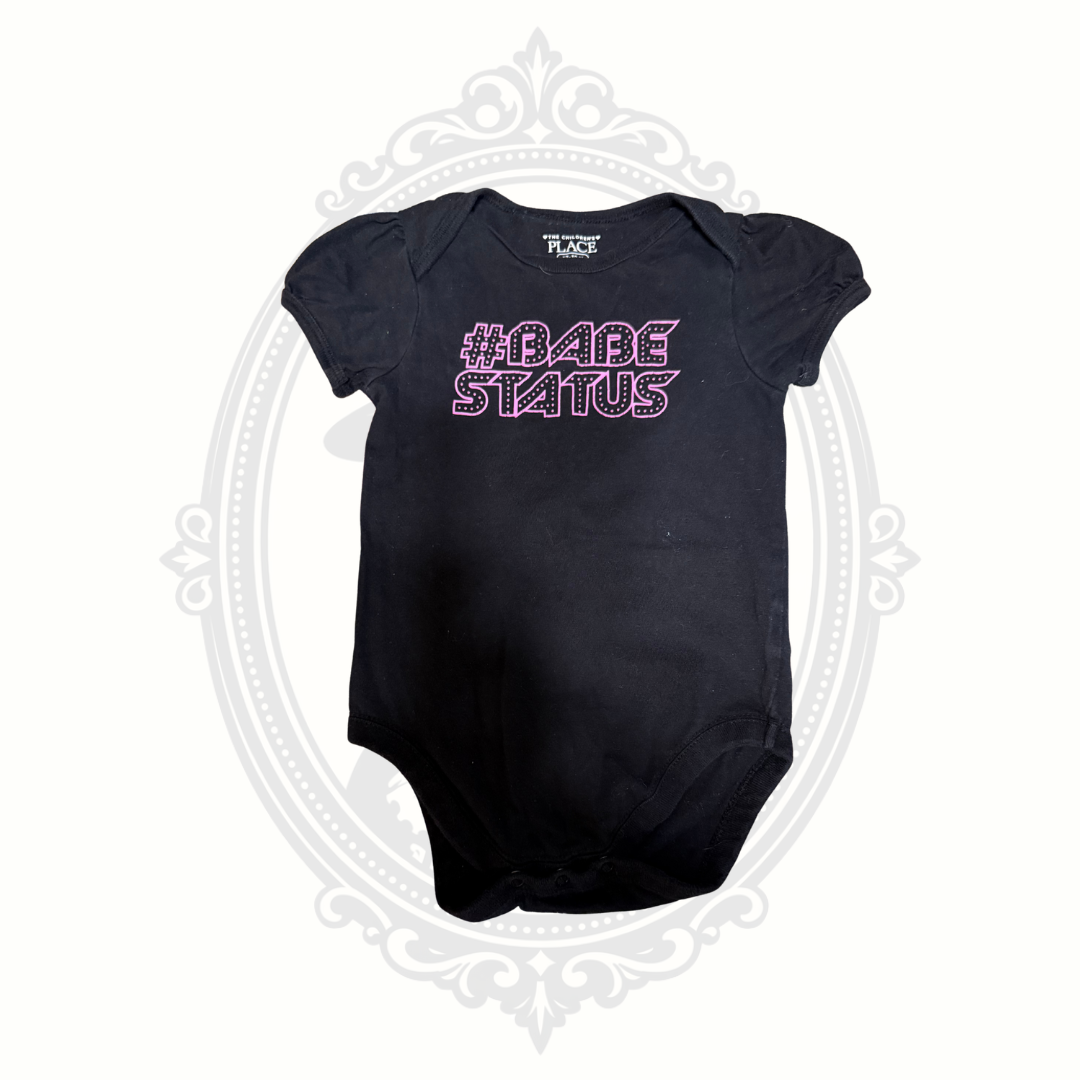 Front view of black baby onesie with pink “#Babe Status” graphic from The Children’s Place.