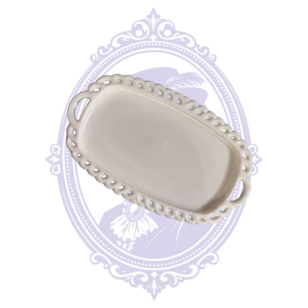 Overhead view of a vintage Colony Harvest white milk-glass creamer and sugar undertray, featuring an oval-shaped recessed center, decorative pierced lace-like border, and integrated handles at both ends. Displayed against the pale lavender Mrs. Bones Curio Cupboard Research Library background.