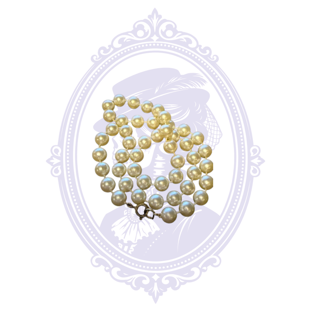 Cream faux pearl costume jewelry necklace arranged to show the round imitation pearls and metal clasp.