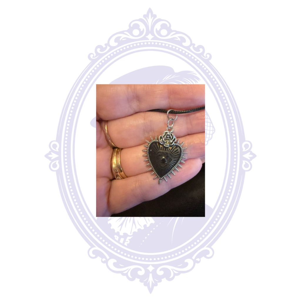 Black-tone Sacred Heart eye pendant with rose detail and small black center stone shown in hand for scale.