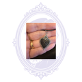 Black-tone Sacred Heart eye pendant with rose detail and small black center stone shown in hand for scale.