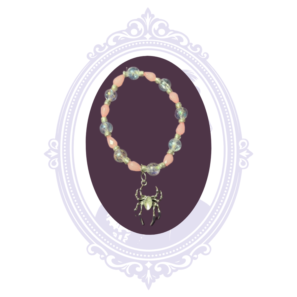 Hand-assembled pink and iridescent stretch bracelet with dangling spider charm shown on a dark purple display.