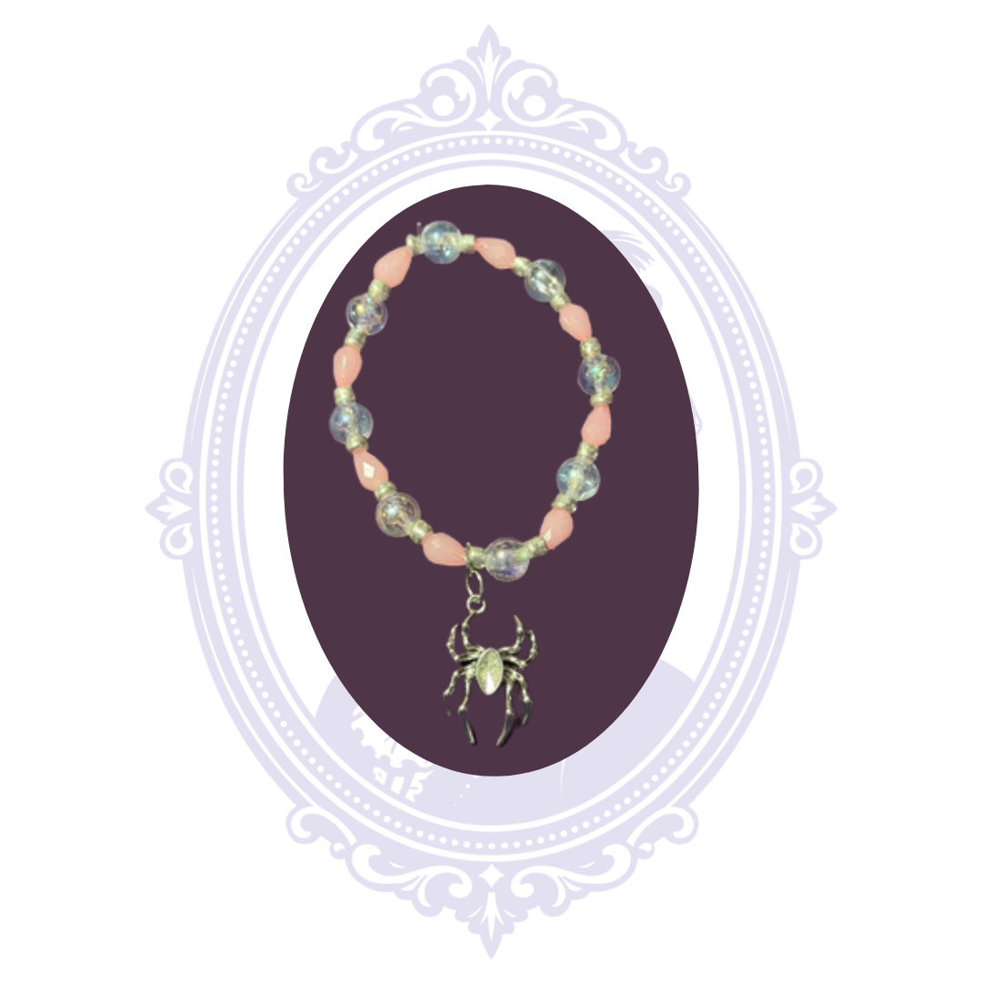 Hand-assembled pink and iridescent stretch bracelet with dangling spider charm shown on a dark purple display.