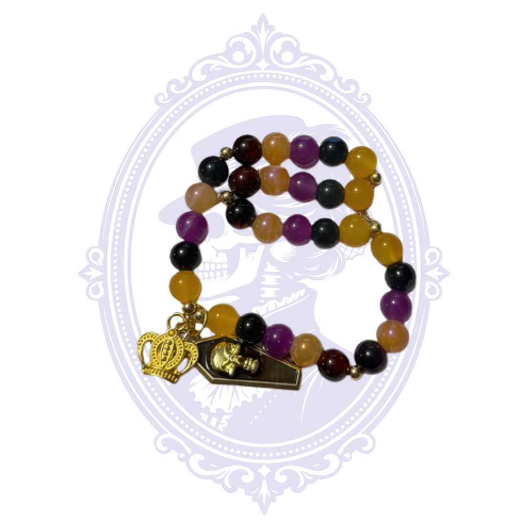 Close view of extra-large multicolor glass bead bracelet with gold-tone crown and crowned skull coffin charms.