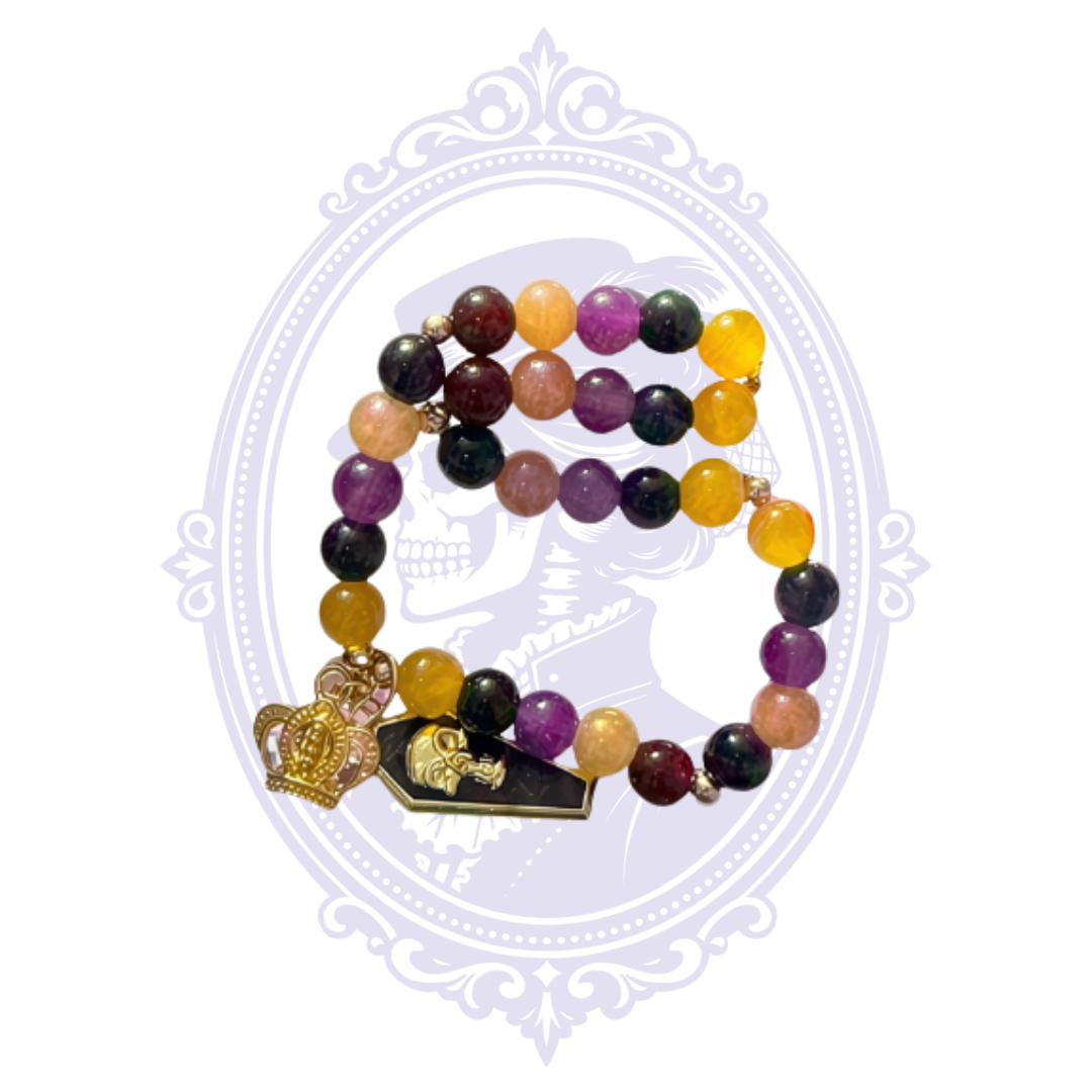 Extra-large purple, black, gold and amber glass bead stretch bracelet with crowned skull coffin and crown charms, packaged on a handmade jewelry card.