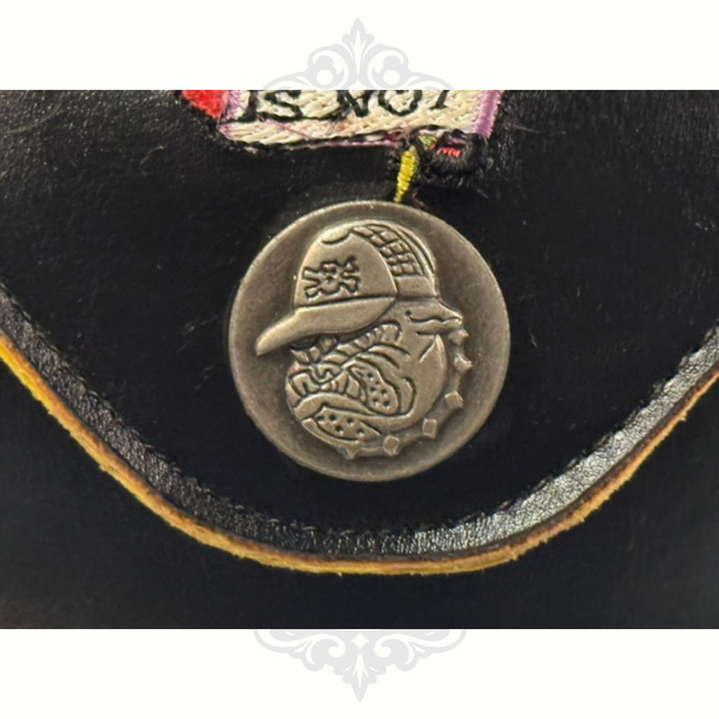 Close-up of a black leather Ed Hardy Sunglasses Case with a decorative snap emblem on a white background