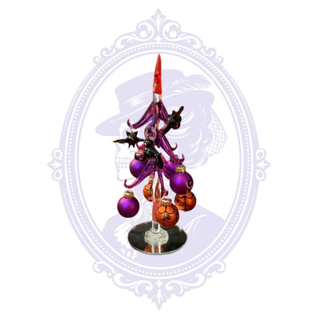 A decorative tabletop Halloween tree ornament featuring a black bat with purple tassels, purple and orange baubles, and a mirrorbase, centered on a white background with a faint ornate frame.
