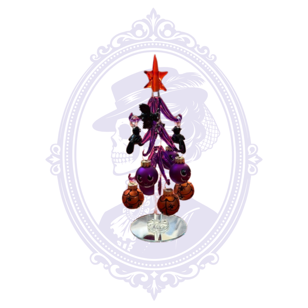 A small decorative Halloween tree with an orange star topper, purple branches, black ornaments, and orange baubles, displayed on a mirror base against a white background with a faint ornate frame.
