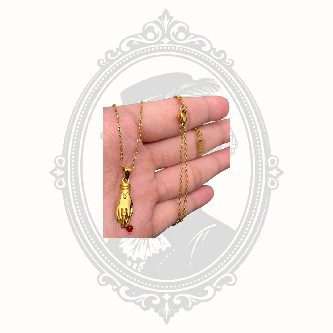 Gold-plated fortune hand pendant necklace with a dangling red crystal heart displayed in hand.