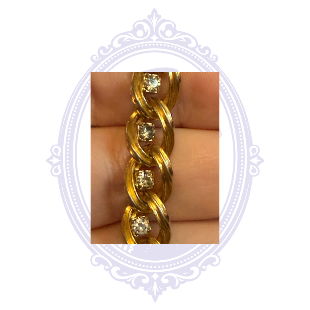 Close-up of clear rhinestones individually set along the links of a gold-tone curb chain bracelet.