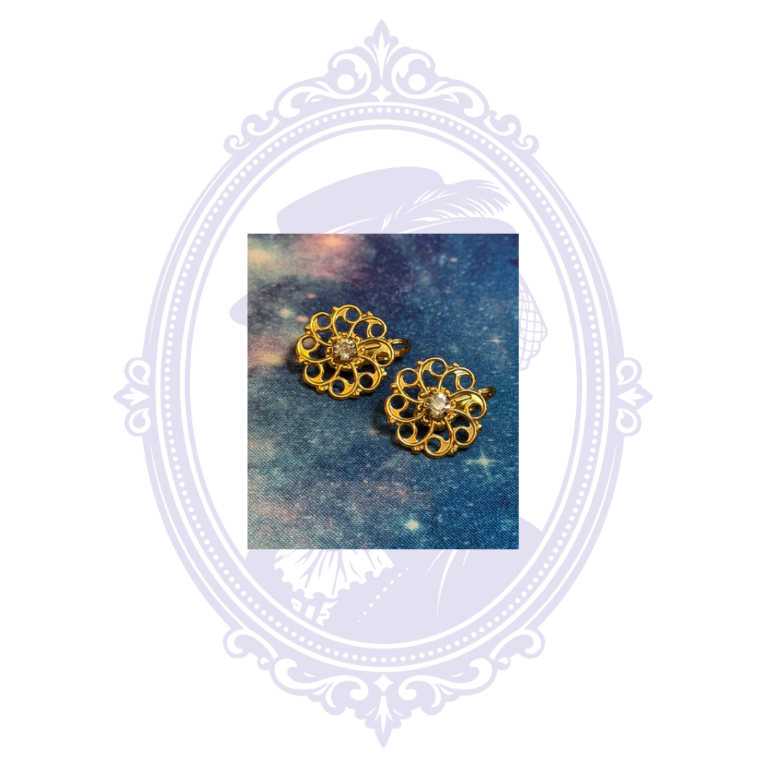 Angled view of gold-tone openwork flower clip-on earrings with sparkling clear center accents.