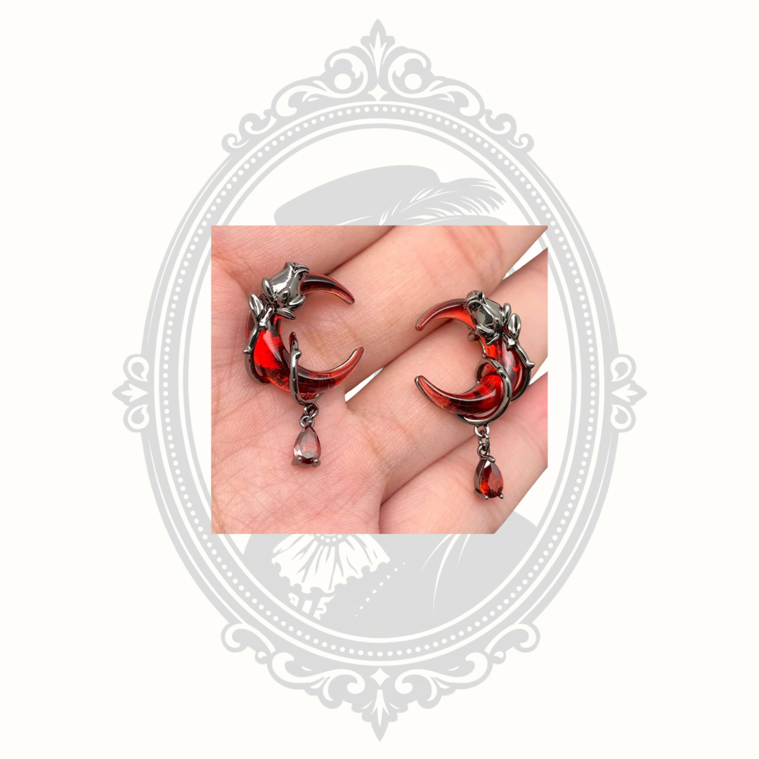 Gothic red crescent moon earrings displayed in hand.