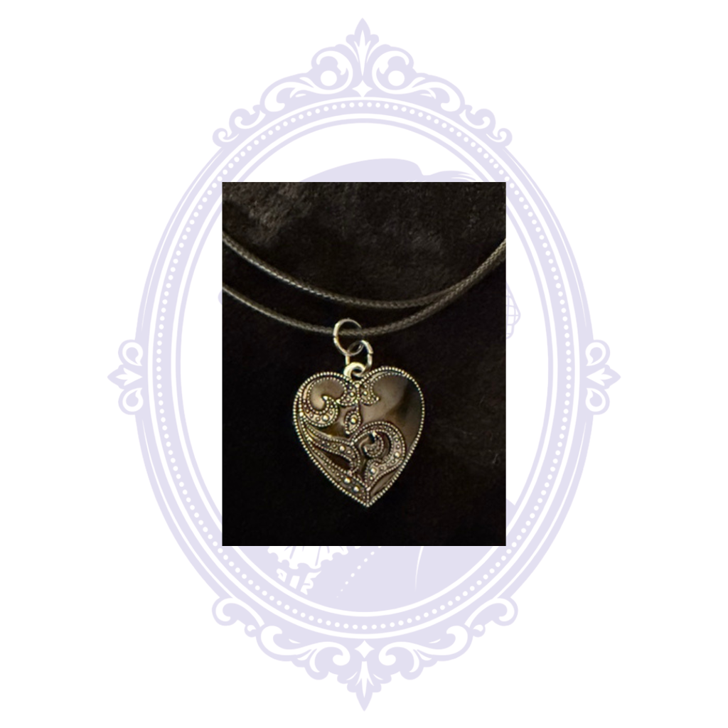 Detailed silver-on-black gothic heart pendant featuring raised swirling scrollwork.