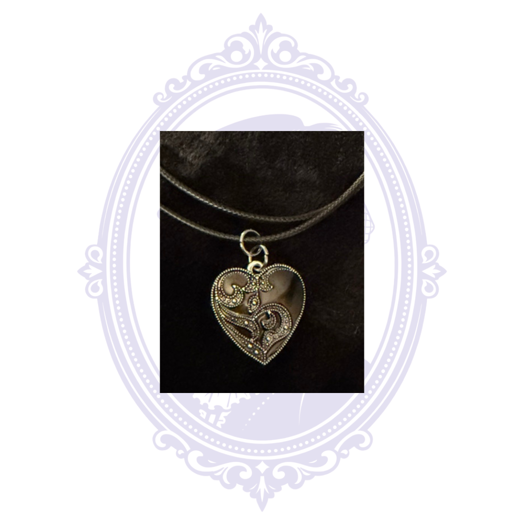 Detailed silver-on-black gothic heart pendant featuring raised swirling scrollwork.