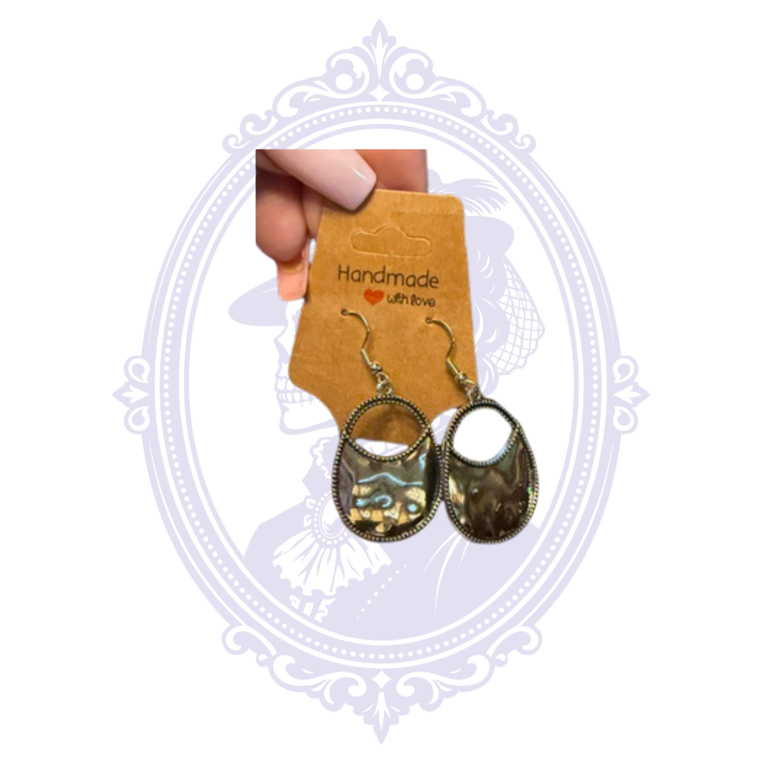 Silver-tone French hook drop earrings shown in hand, highlighting the open oval shape and hammered reflective finish.