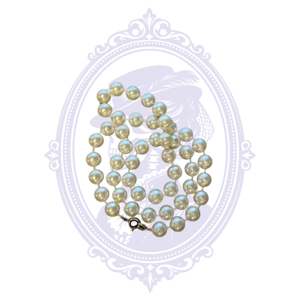 Close-up of ivory imitation pearl necklace showing round faux pearls, individual spacing and metal clasp.