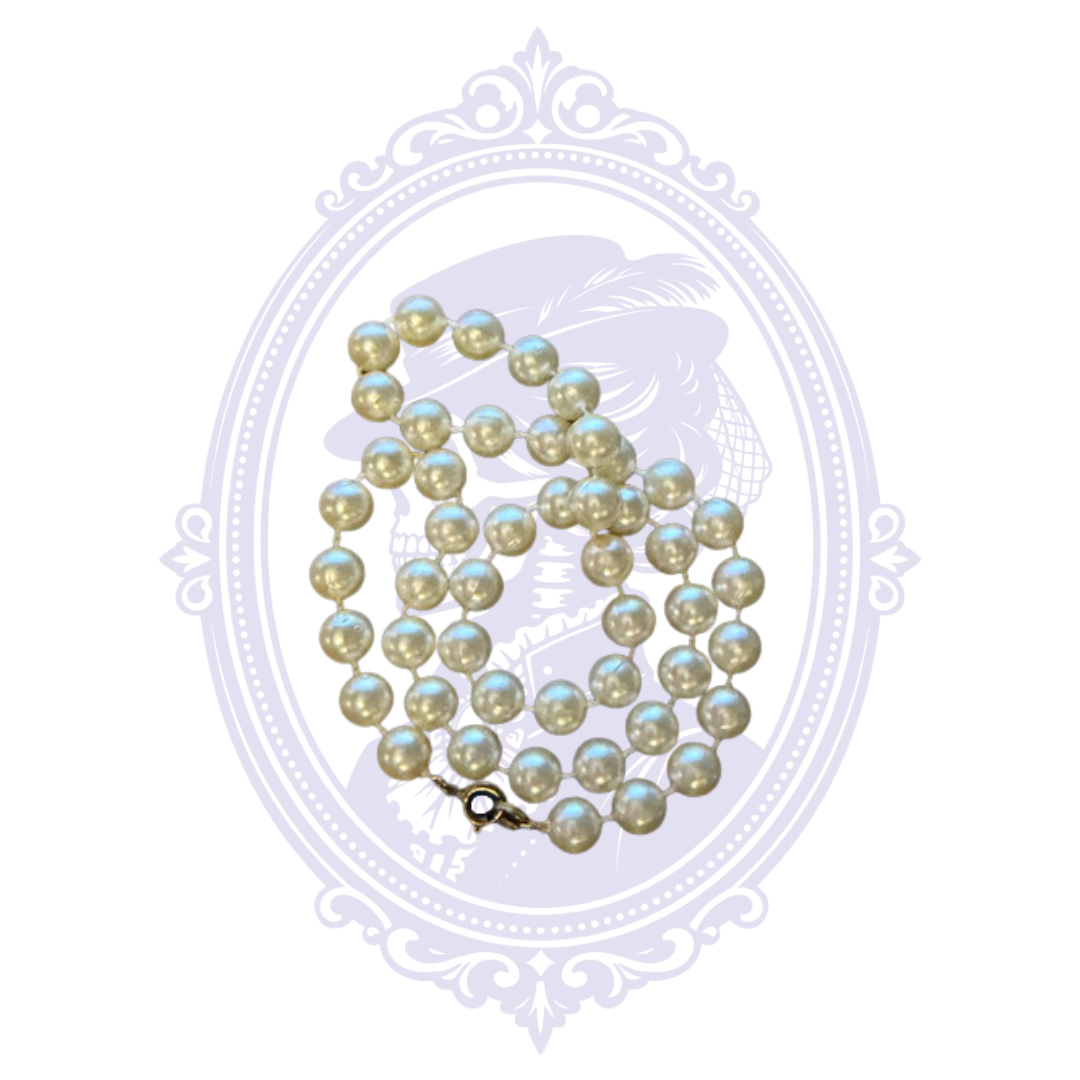 Close-up of ivory imitation pearl necklace showing round faux pearls, individual spacing and metal clasp.