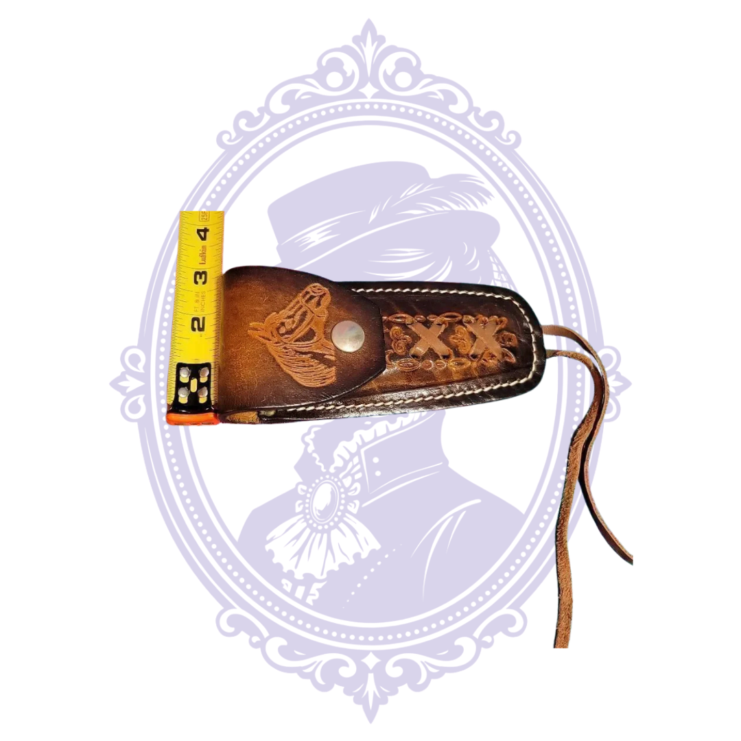 Front close-up of horse-head tooled leather sheath with snap closure and decorative crossed lacing