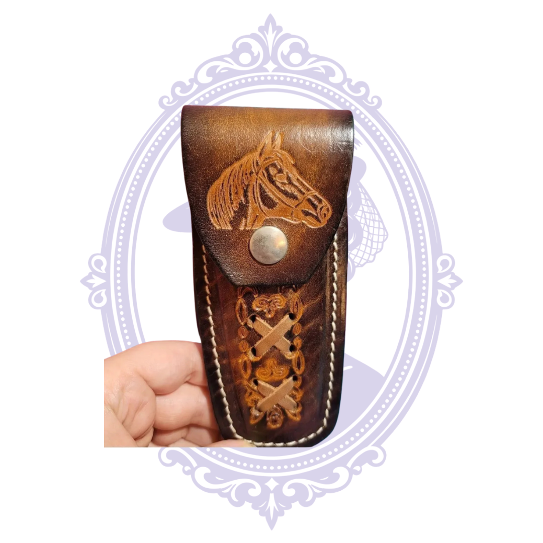 Front view of vintage brown leather belt-loop knife sheath with tooled horse-head snap flap, floral tooling, crossed leather lacing and white stitching