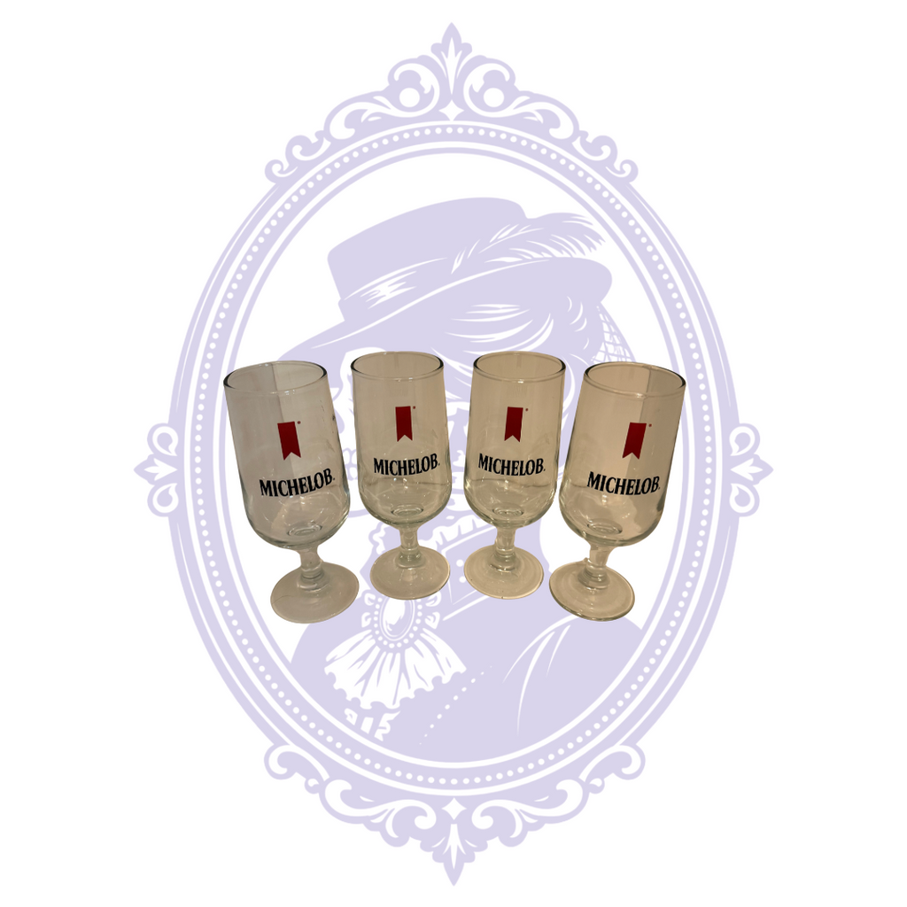 Set of four clear Michelob stemmed pilsner glasses, angled group view showing logos and bases.