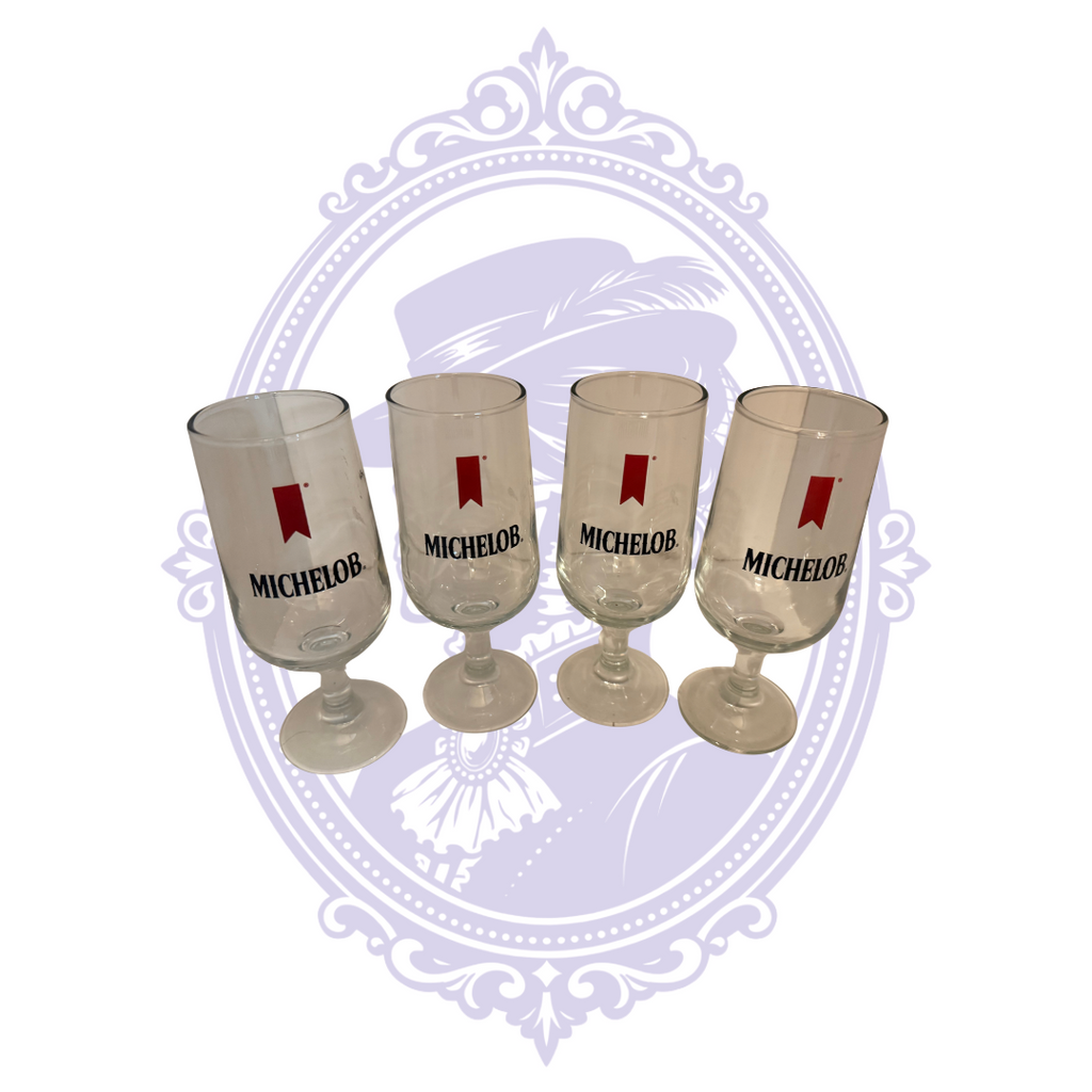 Four Michelob stemmed pilsner glasses with red pennant logos and black Michelob lettering, front view.