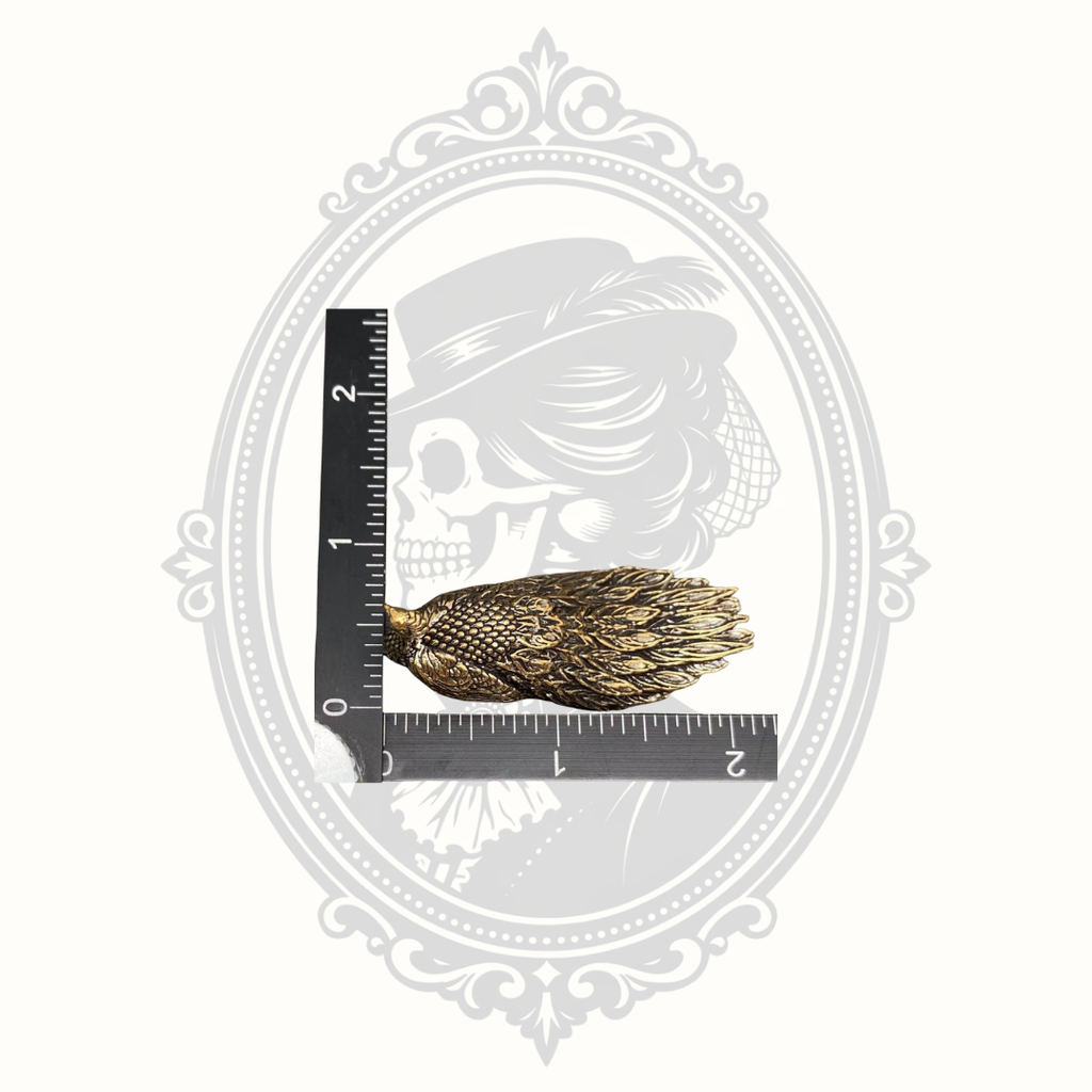 Miniature brass peacock ornament shown beside a ruler for size reference.