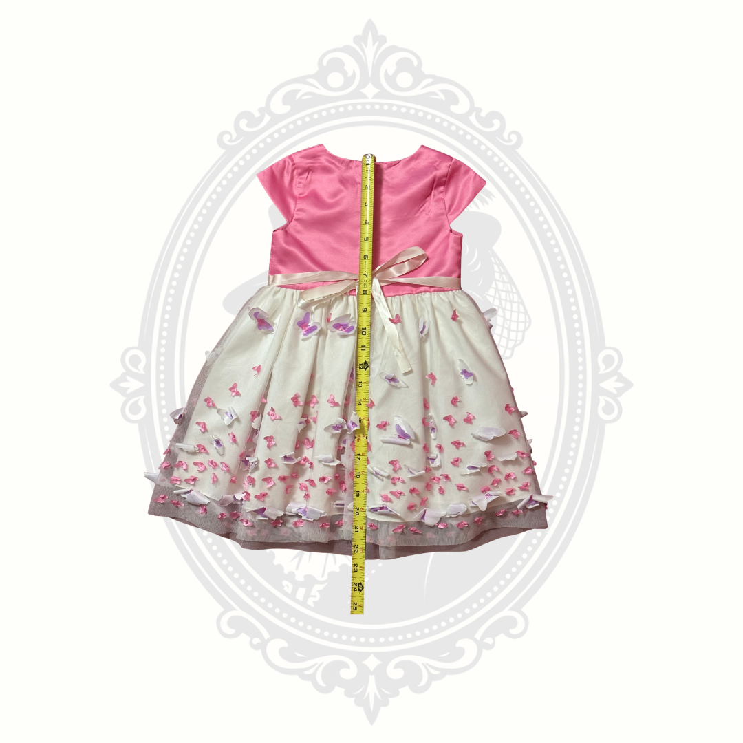 Children's dress with pink top and floral skirt, measured with a tape measure on a white background.