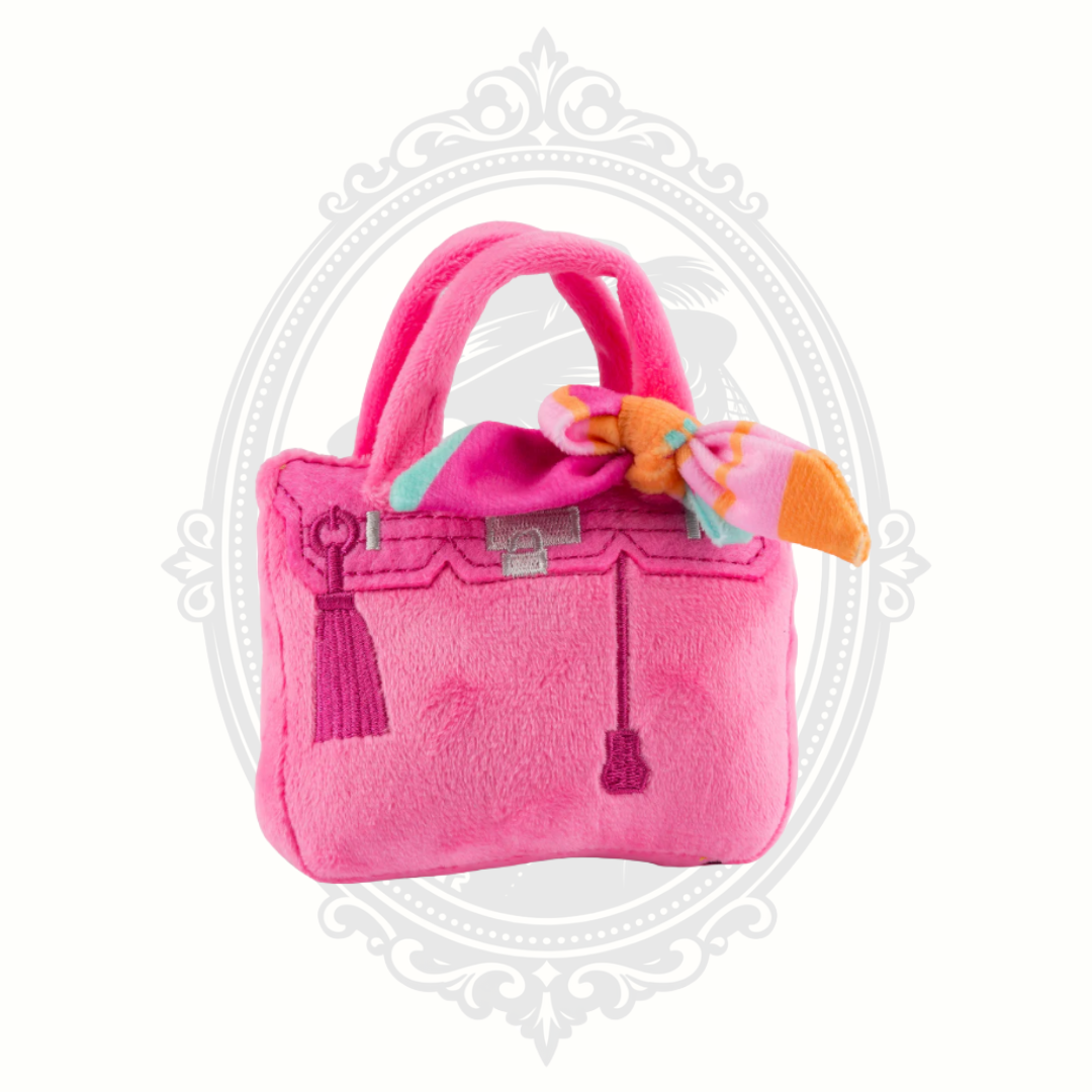 Bright pink plush dog toy handbag with decorative scarf detail and soft carry handles