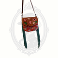 Myra Bag crossbody featuring tooled leather with floral detailing, colorful woven textile body, and long fringe accents.